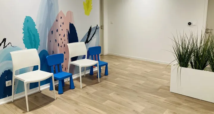 Espace d’accueil du pôle : chaises colorées pour enfants devant une fresque murale, plante verte