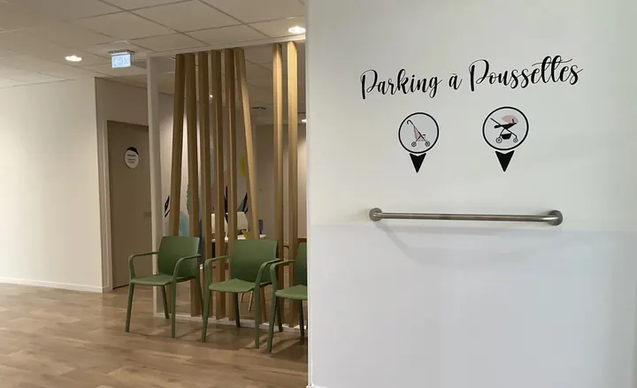 Espace d’attente avec fauteuils verts et inscription « Parking à poussettes »