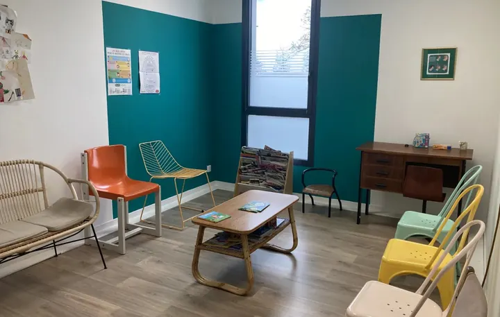 Salle d’attente : mur vert canard, fauteuils colorés, table basse et coin livres